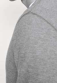 Szary sweter, dziana tekstura, okrągły dekolt i widoczne szwy na ramionach. Naturalny materiał, prosty krój i minimalistyczny styl.