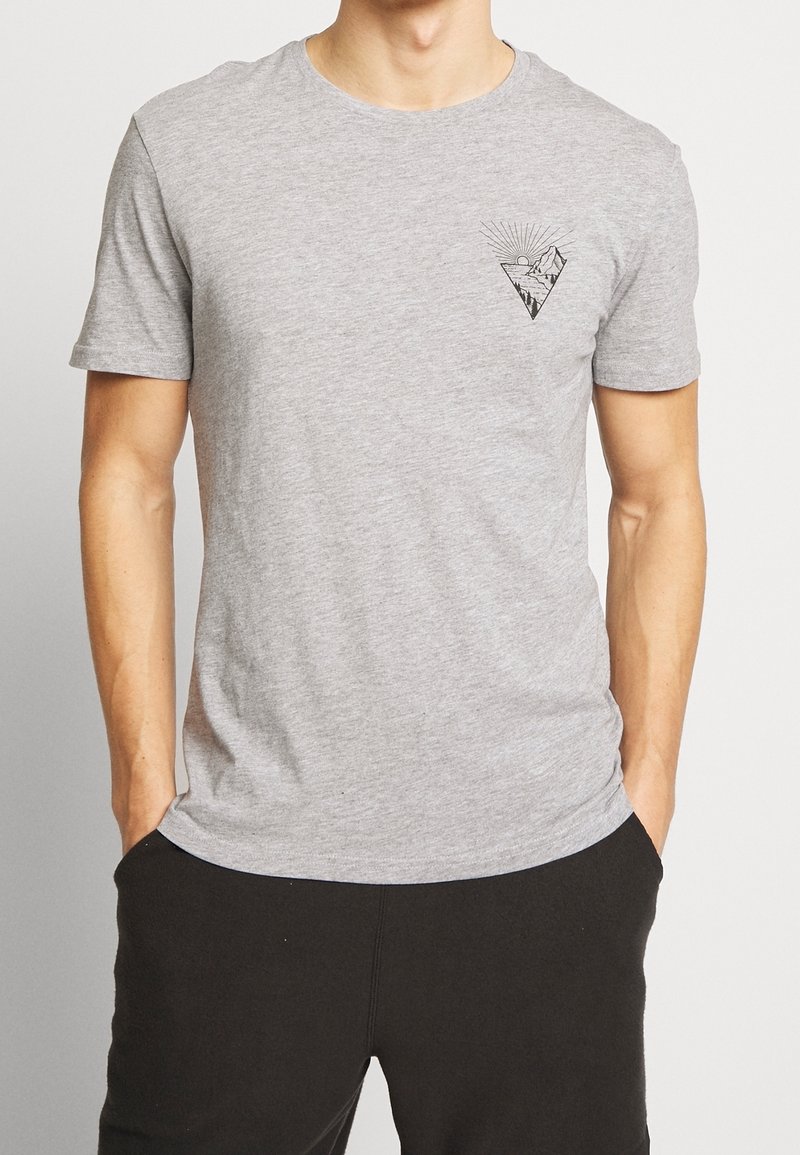 Camiseta de algodón gris con mangas cortas, que presenta un gráfico en forma de triángulo negro en el pecho izquierdo con un diseño de sol y montañas.