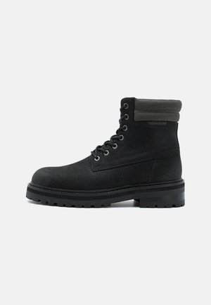 Botte noire montante à lacets avec semelle épaisse crantée et col rembourré, vue de profil sur un fond clair uni.