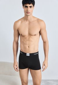 Boxeri negri dintr-un material neted, cu un elastic cu marcă alb, având un design ajustat și aerodinamic.