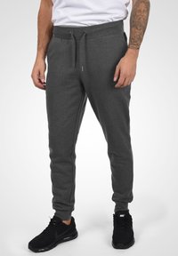 Grå, åtsittande joggers med resårmidja och dragsko, med sidofickor och en slät textur. Kombineras med svarta träningsskor.