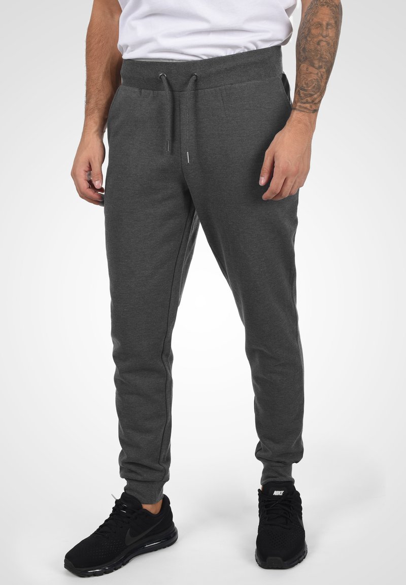 Grå, åtsittande joggers med resårmidja och dragsko, med sidofickor och en slät textur. Kombineras med svarta träningsskor.