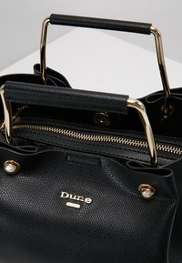 Sort struktureret lædertaske med guldfarvede detaljer, dobbelte håndtag, lynlås lukning og et præget logo på fronten.