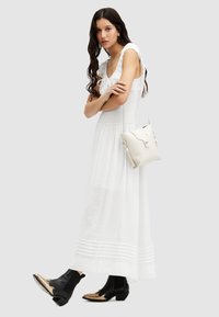 Robe maxi blanche sans manches avec un décolleté volanté et un corsage smocké. Associée à des bottines noires avec un bout métallique. Sac à main léger.