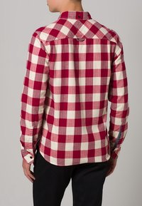 Rood-wit geruite blouse met lange mouwen en een knoopsluiting aan de kraag, voorzien van een achterpand en knoopaccenten op de manchetten.