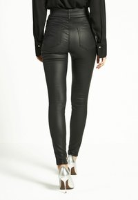 Hoge zwarte faux leren broek met een aansluitend ontwerp, dubbele achterzakken en een gladde textuur. Gecombineerd met metallic hoge hakken.