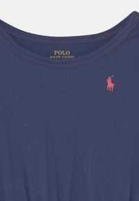 Tummansininen Polo Ralph Lauren -paita, jossa on vaaleanpunainen brodeerattu hevonen ja ratsastaja -logo ylärinnassa.