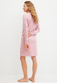 Abito rosa realizzato in tessuto morbido con maniche lunghe, caratterizzato da un motivo a cuori bianchi. Il design include una vestibilità comoda e polsini a costine.