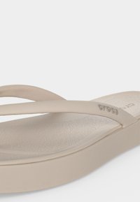Μπεζ σανδάλι Crocs τύπου flip-flop με υφασμένη εσωτερική σόλα και λεπτά λουράκια, ένα λουράκι με ανάγλυφο λογότυπο "crocs".
