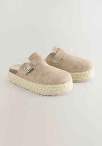 Zuecos de ante beige con una plataforma de yute trenzado y un detalle de hebilla plateada. Diseño de espalda abierta, textura suave, altura de tacón bajo.