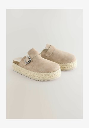 Beige zamša klumpi ar austu jūtu platformu un sudraba sprādzi. Atvērta aizmugure, gluda tekstūra, zems papēža augstums.