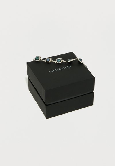 Ασημένιο βραχιόλι με πέντε σκούρες μπλε οβάλ πέτρες, τοποθετημένο πάνω σε μαύρο κουτί κοσμημάτων Nanncrocetti, σε λευκό φόντο.