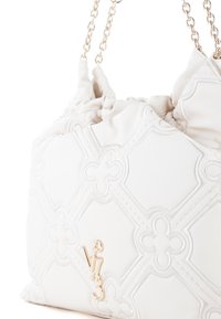 Witte gequiltte handtas met gouden kettinghandvatten. Voorzien van een reliëf bloemmotief en een prominent logo aan de onderkant. Zacht, textuur materiaal.