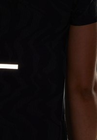 T-shirt nero con motivo a zigzag e una striscia riflettente sulla parte frontale. Maniche corte e tessuto morbido.