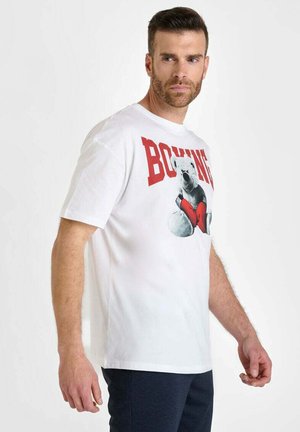 Camiseta de algodón blanca con un gráfico de un oso boxeando con corazones rojos, la palabra "BOXING" en letras rojas en negrita arriba. Mangas cortas, corte holgado.