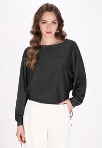 Top nero scintillante a maniche lunghe con scollatura ampia e vestibilità comoda, abbinato a pantaloni bianchi larghi con dettagli in cordoncino.