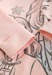 Rausvos spalvos džemperis su grafiniu dizainu, kuriame vaizduojami personažai, minkšta medžiaga, siaurėjančios apačios ir blizgančios blizgučių detalės priekyje.