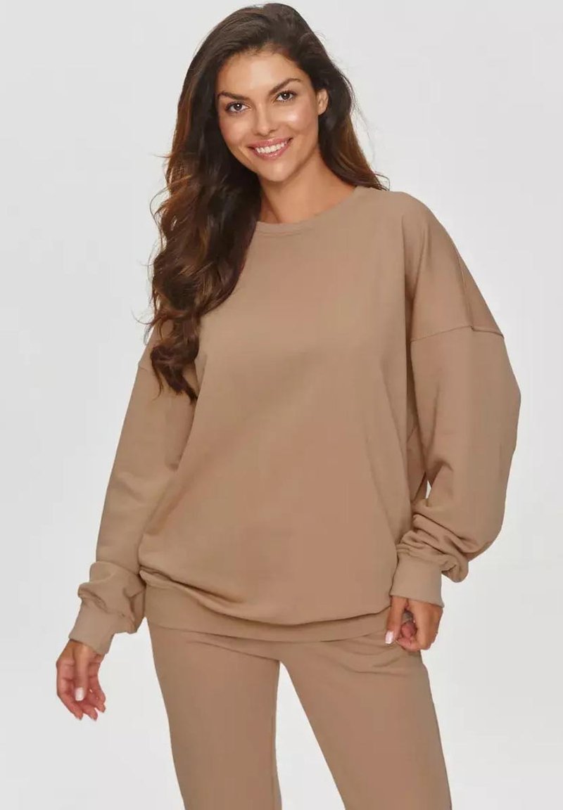 Beżowy, oversize'owy sweter z długimi rękawami, okrągłym dekoltem i ściągaczami, stylizowany z dopasowanymi beżowymi dresami. Miękka tekstura materiału.
