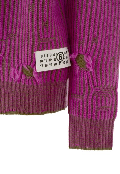 Pull en tricot rose vif et violet, avec des rayures verticales, bords effilochés et une étiquette en tissu indiquant les tailles et les numéros.