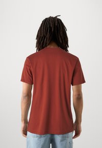 Hrdzavohnedé tričko s krátkym rukávom a klasickým okrúhlym výstrihom, vyrobené z mäkkej látky, s hladkým povrchom a bez viditeľných vzorov.