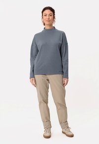 Gray sweatshirt with a high neckline, long sleeves, and loose fit, paired with beige pants. The outfit features minimal design and subtle branding.