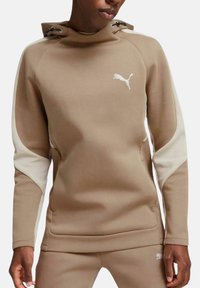 Sudadera beige con capucha, paneles laterales blancos y un pequeño logo blanco de Puma en el pecho. Textura suave y diseño ajustado.