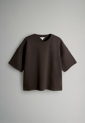 Tmavě hnědé tričko s krátkým rukávem vyrobené z bavlny. Uvolněný střih s kulatým výstřihem a sníženými švy na ramenou, s hladkou strukturou.
