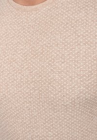 Top color beige claro hecho de una tela suave, con un patrón texturizado de pequeños corazones blancos y un clásico escote redondo.