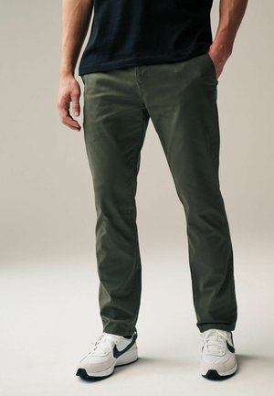 Oliven grønne chinos lavet af bomuldsblanding, med en slim fit, forlommer og baglommer, parret med hvide og sorte træningssko.