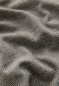 Tissu à carreaux brun et blanc avec un motif pied-de-poule présenté en plis doux et détails de texture.