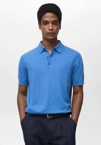 Polo de culoare albastră, cu mânecă scurtă, realizat dintr-un material neted, având guler și clapetă cu două nasturi. Purtați cu pantaloni închiși la culoare.