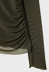 Olivenfarvet gennemsigtig skjorte med rynkede detaljer langs siden, der har en blød tekstur og et flydende design med en let frynset kant.