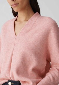Rosa V-Ausschnitt-Pullover aus weichem, strukturiertem Stoff mit lockerer Passform und weiten Ärmeln, ausgestattet mit einem dezenten Melange-Muster.
