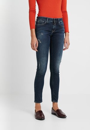 Donkerblauwe skinny jeans van denim, met een gemiddelde taille, lichte distressed details en een slim-fit ontwerp. Gepaarde met bordeauxrode instappers.