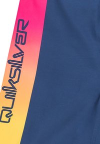 Marina simbyxor med en gradient från rosa till orange på sidopanelen. Har en svart "Quiksilver"-logotyp längs sömmen för profilering. Slät textur.
