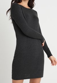 Abito grigio a maniche lunghe realizzato in un morbido tessuto testurizzato. Presenta un collo rotondo e una silhouette aderente che si ferma sopra le ginocchia.