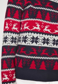 Röd, vit och marinblå mönstrad stickad tröja med renar, träd och geometriska former. Ribbad ärm och nederkant med en mjuk textur.
