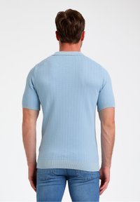 Gaiši zila īsām piedurknēm polo krekls, teksturēta dzijas auduma, ribotas aproces un apakšmalas, līdzens apkakle, skatīts no aizmugures uz modeli.