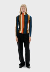 Rullekrave top med lodrette striber i brun, blå, orange og creme. Figurformet design kombineret med løsthængende sorte bukser og flade sko.