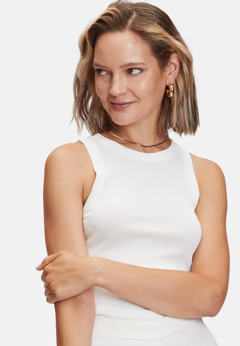 Witte geribde tanktop met een aangesloten ontwerp, voorzien van een ronde halslijn en mouwloos. Het model heeft schouderlang haar en draagt gouden accessoires.