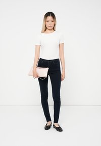 Fehér, rövid ujjú felső, sötét skinny farmernadrág, fekete lapos cipő és rózsaszín táska lánc részlettel. Egyszerű és illeszkedő sziluett.
