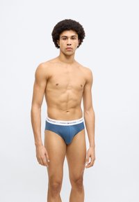 Ανδρικά εσώρουχα σε σκούρο μπλε ύφασμα με λευκή ελαστική ζώνη μέσης με λογότυπο. Διαθέτουν στενή εφαρμογή και λεία υφή.