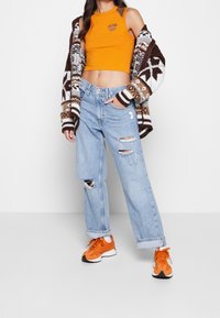 Orange crop top, mönstrad brun och vit cardigan, ljusblå ripped jeans och orange sneakers med vita och svarta accenter.