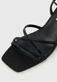 Sandales noires à lanières avec un bout carré, finition mate élégante et cristaux noirs brillants le long des lanières pour accentuer le tout.