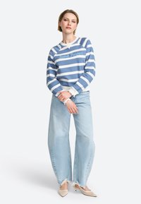 Felpa a righe blu e bianche con colletto a girocollo e logo, abbinata a jeans a gamba larga blu chiaro con orli sfrangiati.