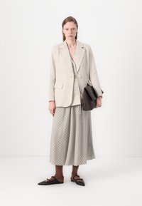 Beige linblazer over en knappet vest, kombinert med et stripete maxiskjørt og mørke sko. En brun skulderveske fullfører antrekket.