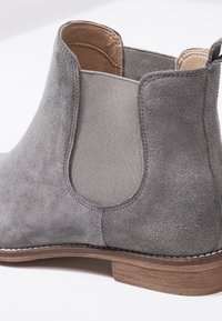 Bottine Chelsea gris en daim avec panneau latéral élastique et semelle en bois sur fond blanc.