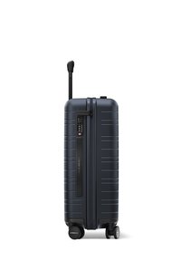 Valise rigide de couleur bleu marine foncé avec une surface texturée, poignée extensible, serrure à combinaison et deux roues lisses pour une mobilité aisée.