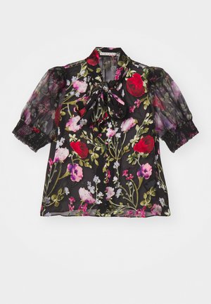 Svart genomskinlig blus med blommönster. Har puffärm, en rosett runt halsen och spetsdetaljer vid ärmsluten.