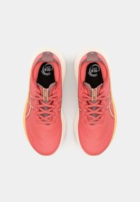 Chaussures de sport rouges avec une tige texturée, une semelle claire contrastante et des accents orange subtils. Elles possèdent un laçage traditionnel et un col rembourré.